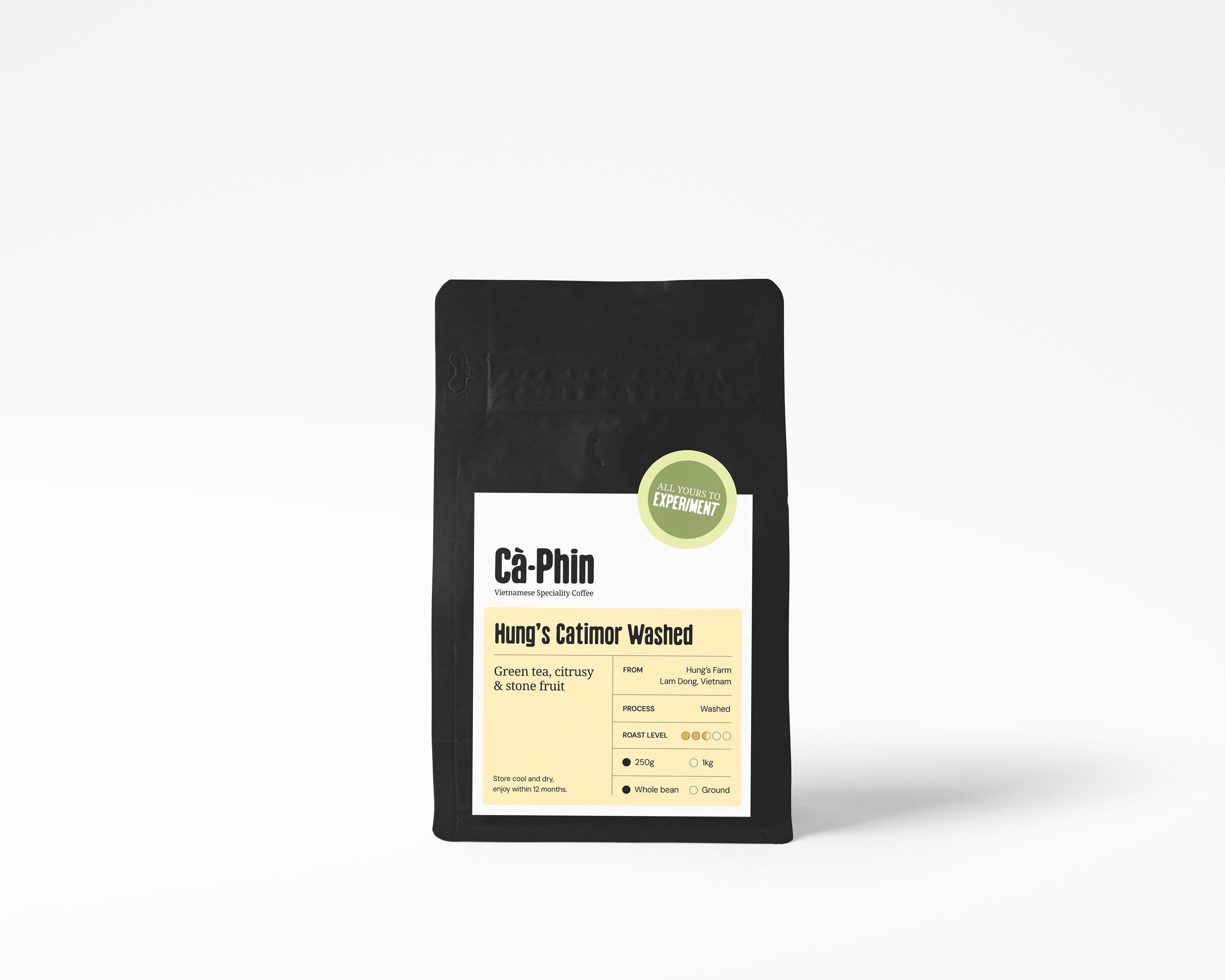 A black stand-up pouch of coffee centered on a light gray background. The front label reads 'Ca Phin Vietnamese Speciality Coffee' and 'Hung's Catimor Washed,' with a small green circular badge near the top right of the label reads 'All Yours to Experiment'.